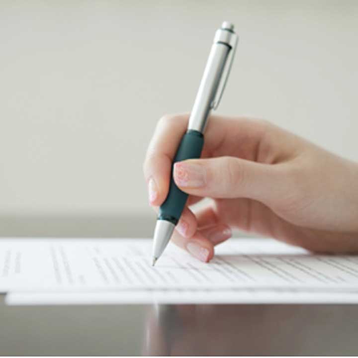 Person signing a contact on a sheet of paper with a green pen