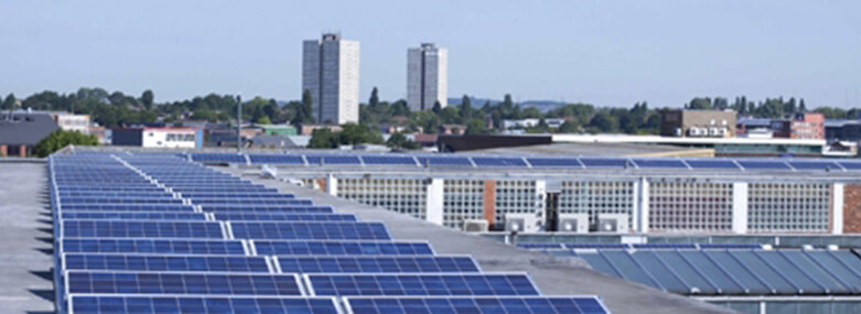 solar panels on the roof of a building with two residential tower blocks in the background