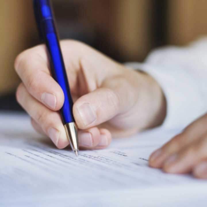 close up of a man's hands writing on paper with a blue pen