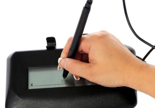 A woman's hand signing an electronic signature pad.