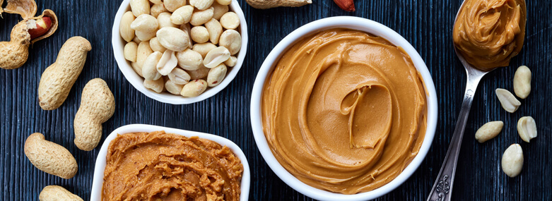 Two bowls of peanut butter and peanuts on dark wooden background