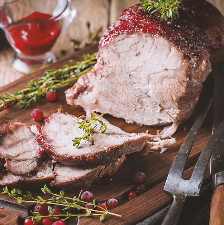 Cooked Pork with cranberry sauce and thyme over wooden background.