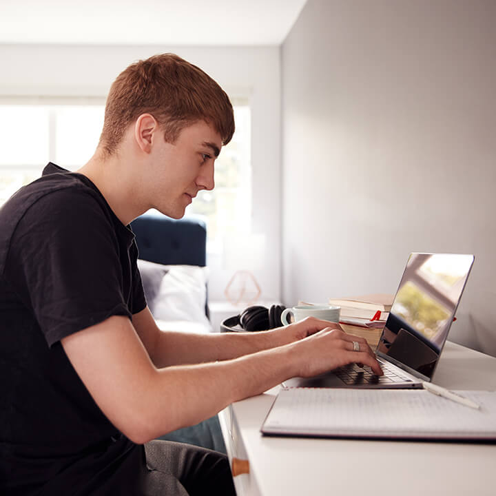 Male College Student In Shared House Bedroom Studying Sitting At Desk