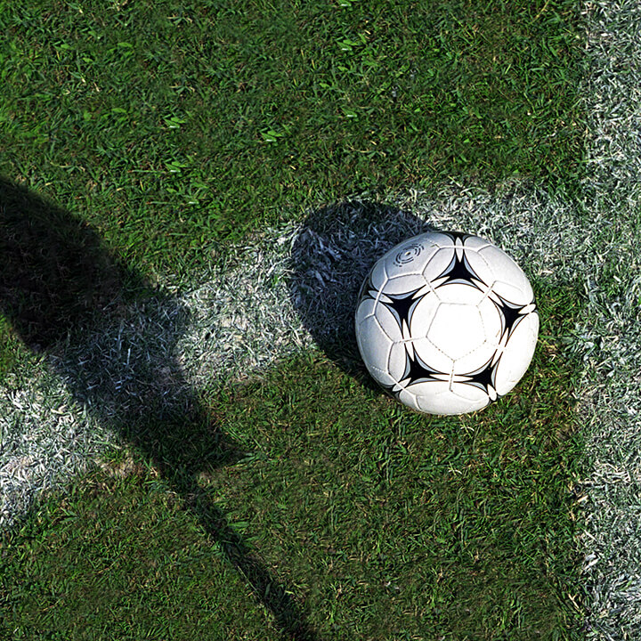 Football on grass by pitch marking and shadow of flag