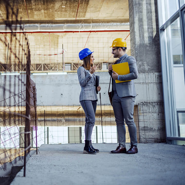 two-colleagues-with-helmets-on-heads-standing-in-building-in-construction