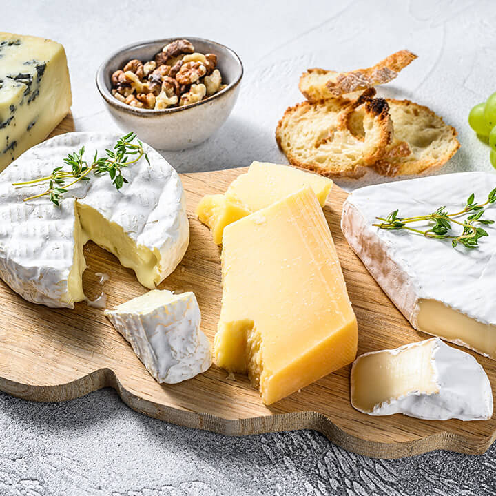 Assorted-cheeses-on-a-wooden-cutting-Board.-Camembert-brie-Parmesan-and-blue-cheese-with-grapes-and-walnuts