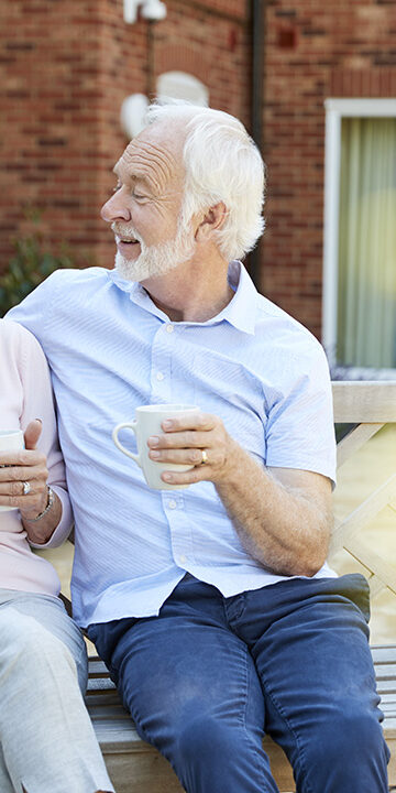 Retired Couple Sitting On Bench With Hot Drink In Retirement home