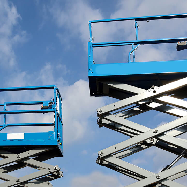 Two working platforms, called scissor elevator, against blue sky with clouds.