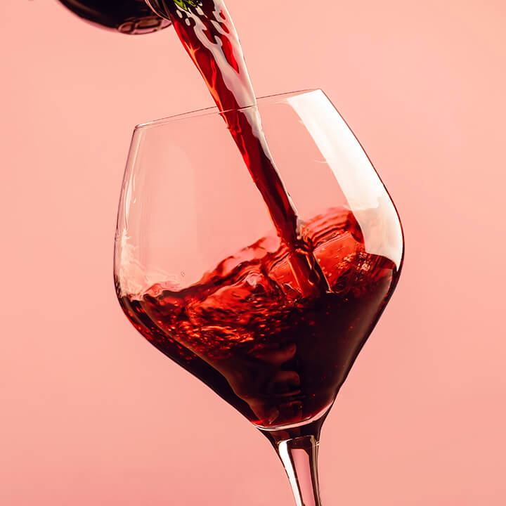 An image of a glass of red wine being poured against a pink background. A visual prompt for this article about wine e-label.