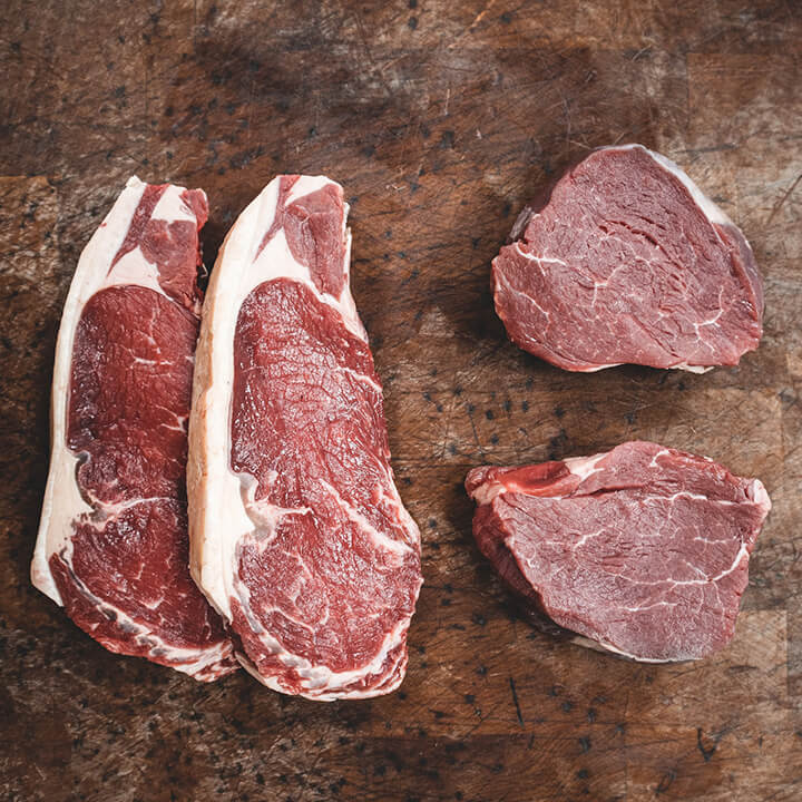 An image of four meat steaks on a wooden chopping board. The article is about food fraud which can include meat items not described accurately.
