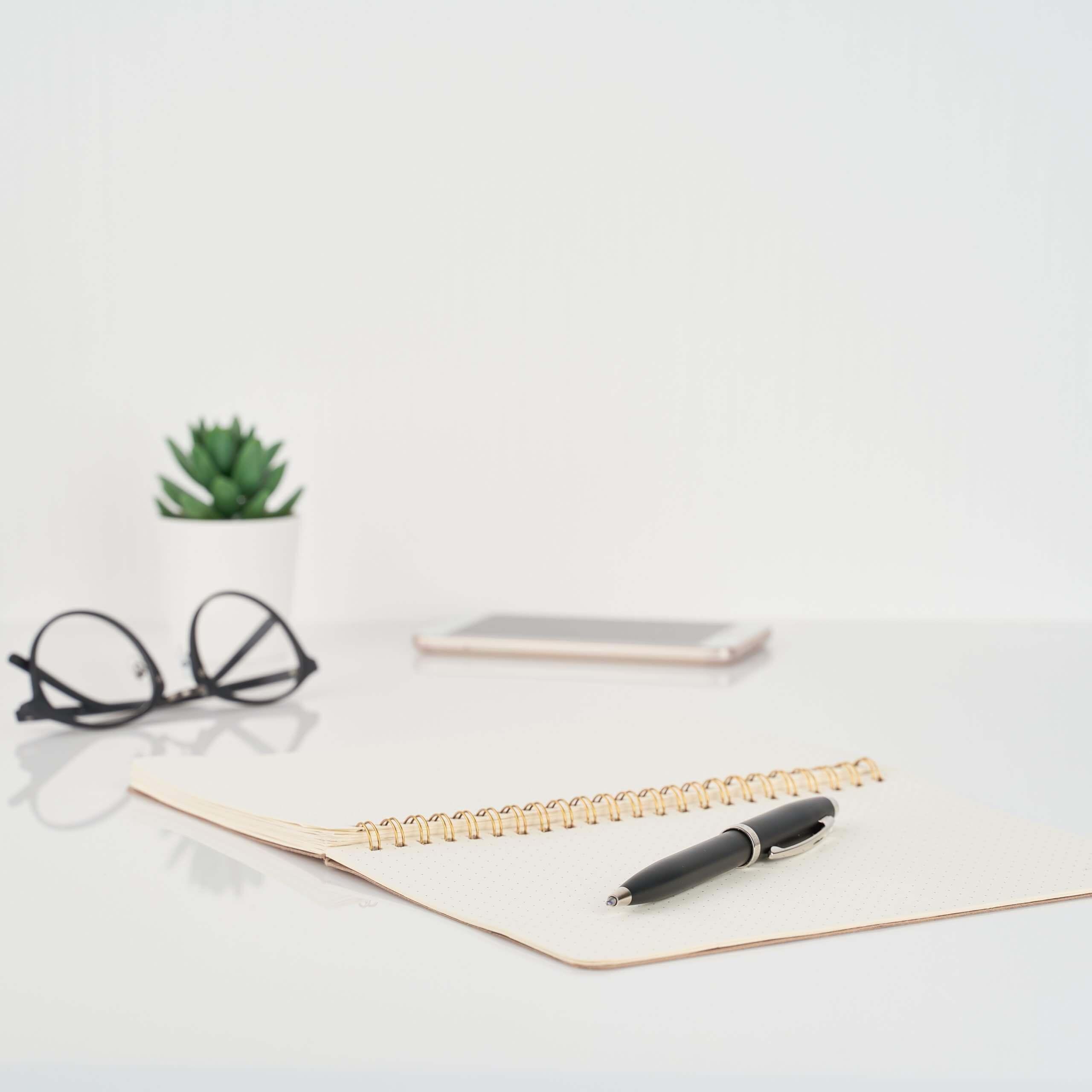 A set of desktop objects, glasses, pad, pen, phone. A visual metaphor for the topic of this article The benefits of obtaining a sponsor licence