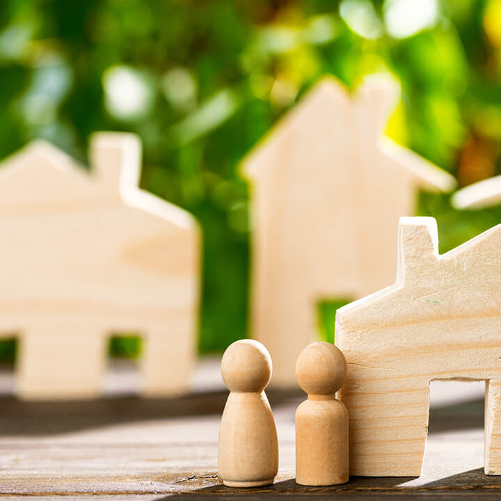 An image of some wood blocks shaped like houses and and two human like figures in front of a leafy garden background. A visual metaphor for the topic of this post, ESG and real estate.