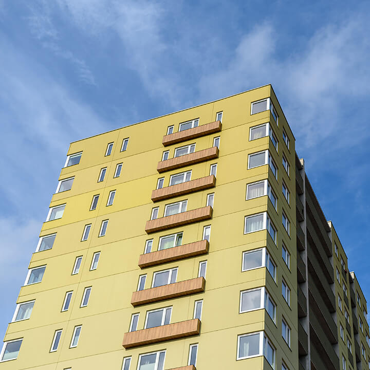 An image of an apartment block, its cladded lime green, against a blue sky and clouds. A visual metaphor for the topic of this article, remediation orders